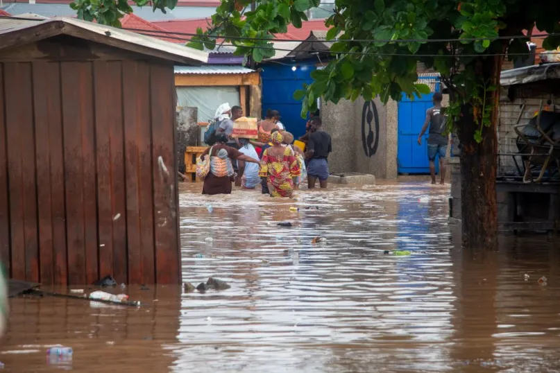 Flooded street in Ghana with houses and people wading through water.