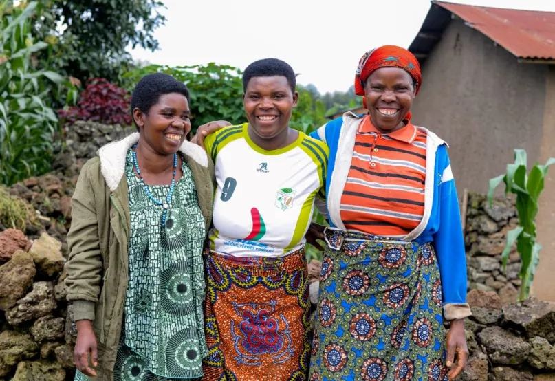 Three Rwandan women smallholder farmers with their arms around each other, smiling.