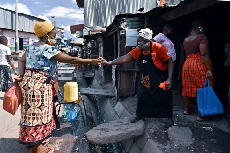 Two women in Nairobi slum reaching out their hands towards each other to exchange money at a safe distance during COVID-19.