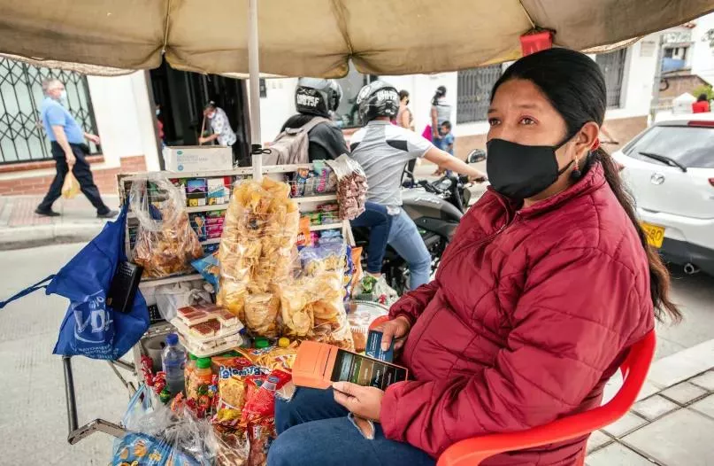 Mujer sentada en su puesto de venta callejero con un POS en sus manos, en Colombia.