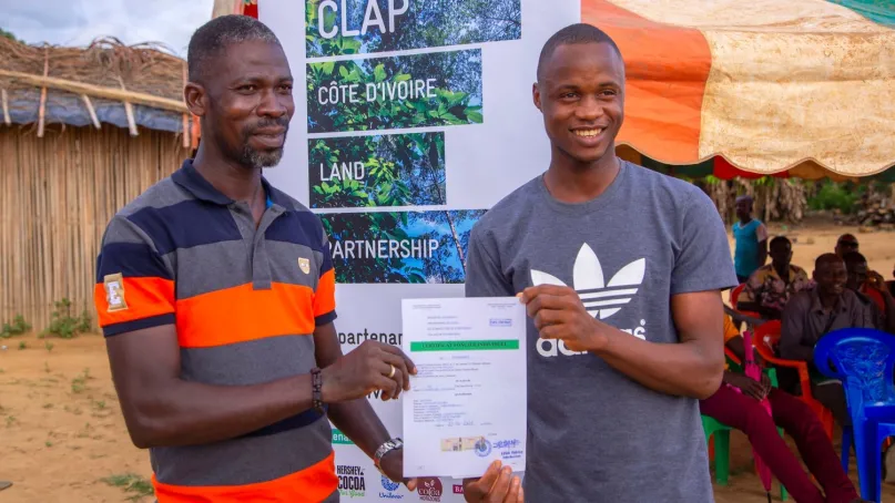 Two cocoa farmers holding up their document.