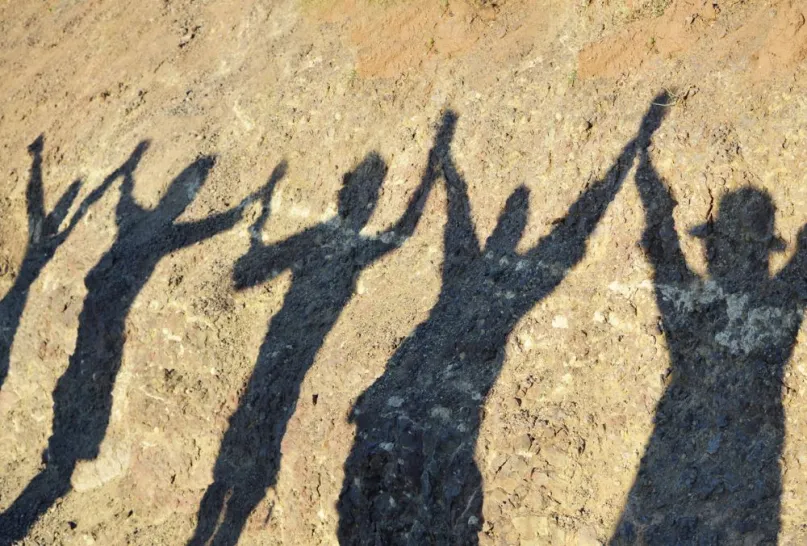 Shadows of four people holding their hands up together.