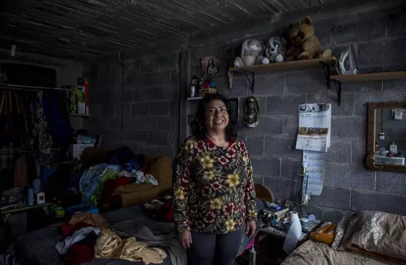 Mujer parada sonriendo a la cámara en el interior de su casa en México.