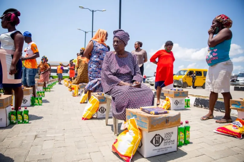 Women in Nigeria standing and sitting in line with bundles of food items.