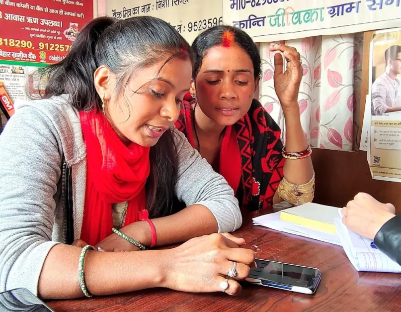 Two women looking at a phone on a desk in India.
