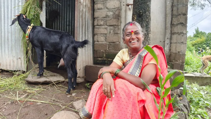 Smiling woman sitting down next to a black goat, India.