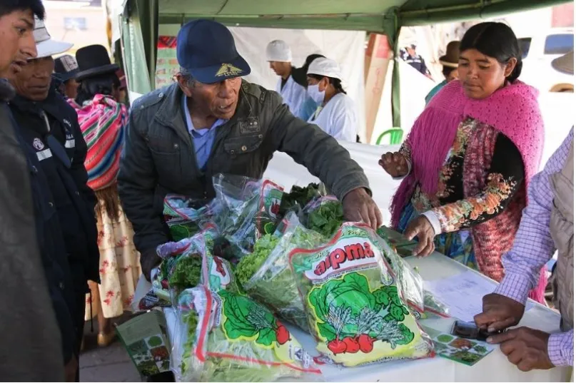 Hombres y mujeres en torno a una mesa de venta de verduras en Bolivia