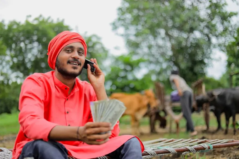 Man with red turban holding phone to ear and holding currency.