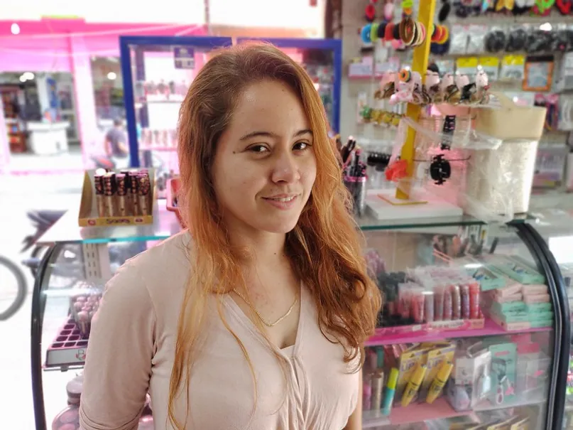 Mujer sonriendo frente a su pequeño comercio.