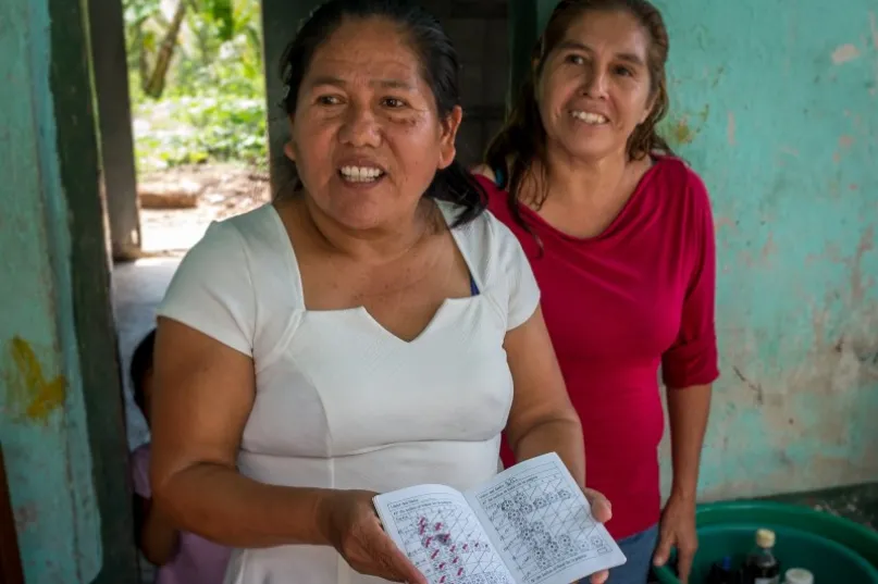 Dos mujeres miran a la cámara, una muestra su libro de ahorros, en Pahuatlan, Puebla, México.