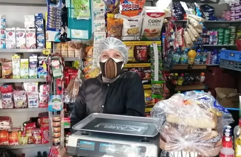 Mujer de tapabocas detrás del mostrador de su pequeño comercio en Perú.
