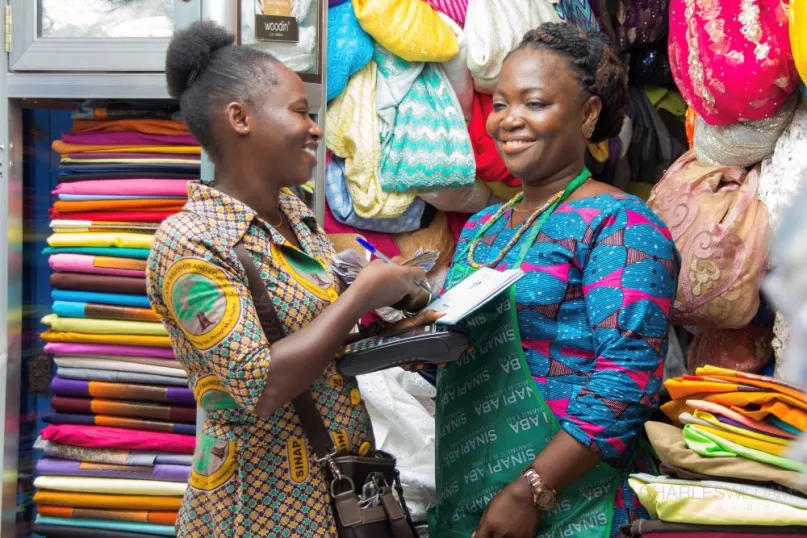 Two women conducting a financial transaction in a shop surrounded by colorful fabrics