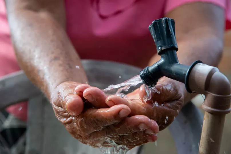A person rinsing their hands with water from an outdoor faucet