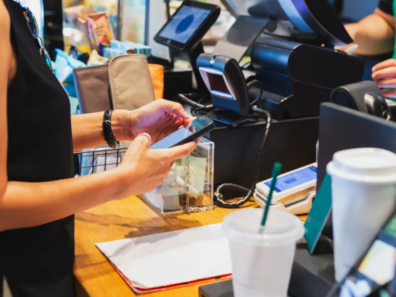 امرأة تقوم بمسح رمز الإستجابة السريعة للدفع عبر الهاتف المحمول أمام أمين صندوق في مقهى.