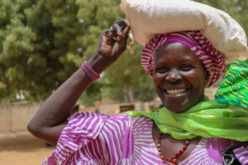 Woman from Senegal smiling and holding a burlap bag on her head.