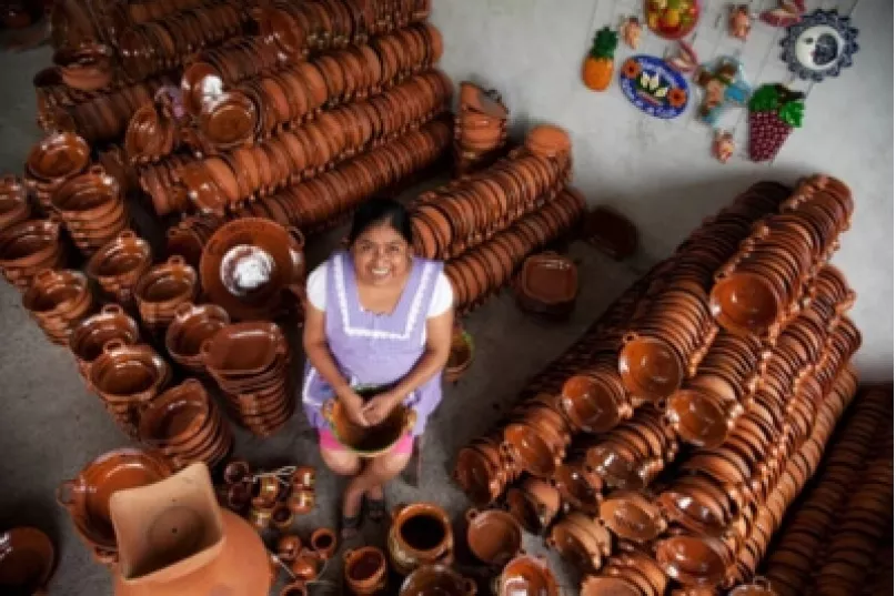 Mujer sentada entre sus vasijas artesanales en México.