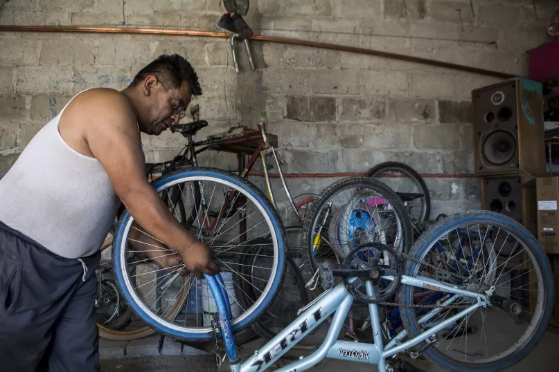 Hombre de musculosa inclinado sobre una bicicleta, arreglando una rueda.