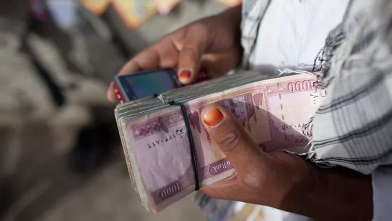 لقطة عن قرب لمرأة تحمل مبلغ نقدي بيد وهاتف محمول باليد الأخرى.