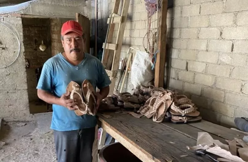 Hombre parado con zapatos en la mano en su taller de calzado artesanal en México.