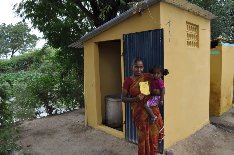 A woman holding her child in front of the toilet in her home in India. Photo Credit: Water.org.