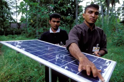 رجلان يحملان لوحًا شمسيًا لاستخدامه في إضاءة منزل قرية في سريلانكا.