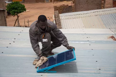 Homme entretenant panneau solaire sur un toit au Mali.