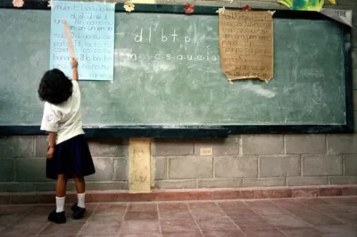 Niña de espaldas escribiendo en un pizarrón en una clase en Honduras.