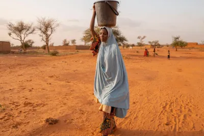Woman walking in desert area holding a bucket on her head