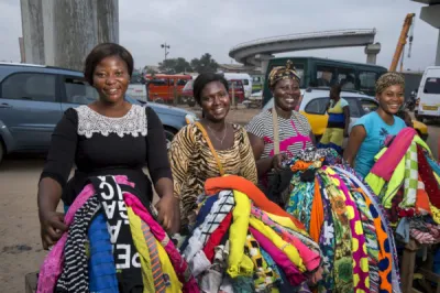 Four women clothing vendors in Ghana sitting and smiling with their wares.