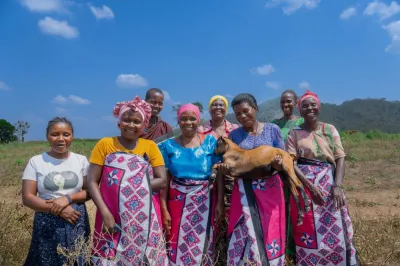 Group of women in a field in Tanzania, smiling, with one holding a goat.