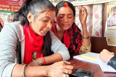 Two women looking at a phone on a desk in India.