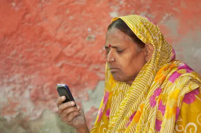 Indian woman in yellow sari looking at a feature phone.