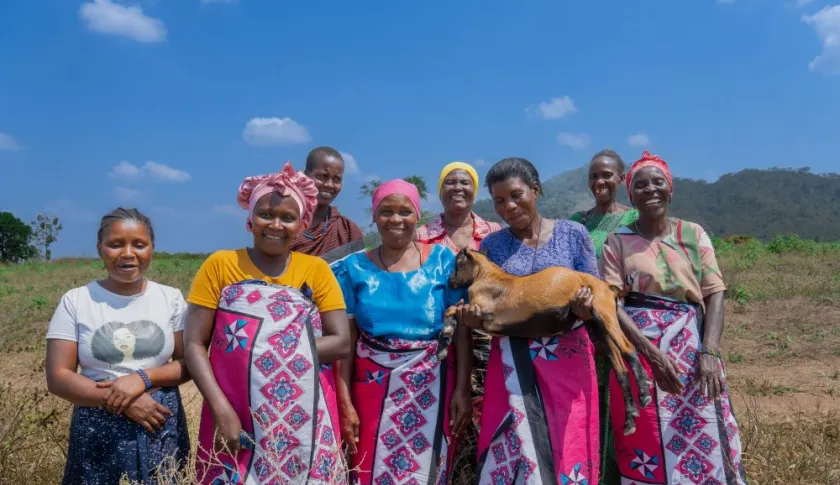 Group of women in a field in Tanzania, smiling, with one holding a goat.