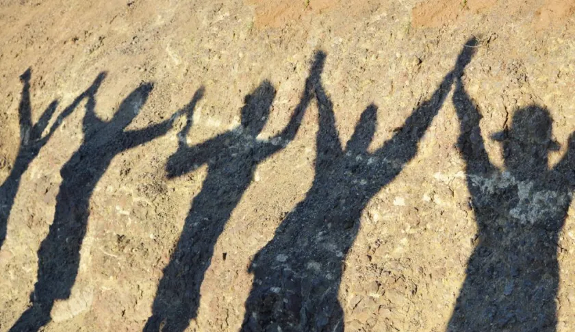 Shadows of four people holding their hands up together.