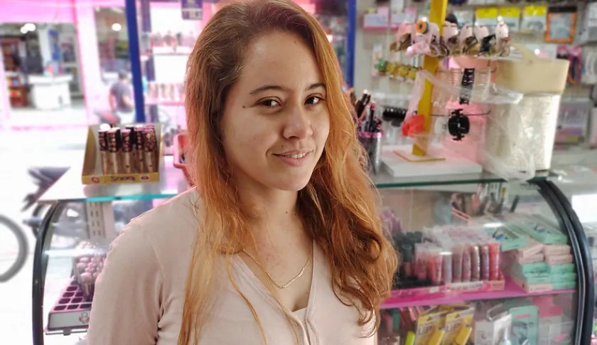 Mujer sonriendo frente a su pequeño comercio.