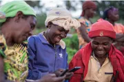 Three women smiling and looking at phones, in a savings group in Rwanda.