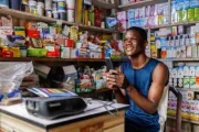 Young man smiling and holding a mobile phone, sitting down in a shop in Nigeria.