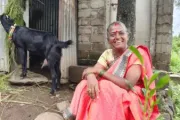 Smiling woman sitting down next to a black goat, India.
