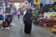 إمرأة تسير في سوق في القاهرة في نوفمبر/تشرين الثاني 2022 حاملة بيدها باقة من الخضار وباليد الأخرى عصاة ومحملة على رأسها كيس من القماش للمونة.