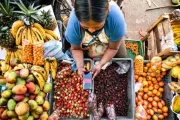 Mujer mirando un celular sobre las frutas y verduras de su puesto en Colombia.