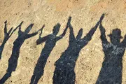 Shadows of four people holding their hands up together.