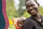 A woman with a baby on her back smiles