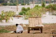 رجل بلباس أبيض يعمل في أرض فيها نبات متناثر في السودان وإلى جانبه عجلة يجر عليها أغراضه.