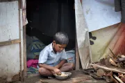 ولد أمام خيمة في مكان متواضع يأكل من على الصحن أمامه على الأرض. 