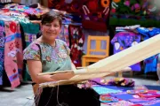 Mujer sentada tejiendo en un telar entre artesanías textiles en México.