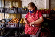 Mujer de barbijo con las manos en su delantal, en su puesto de frutas y verduras en Colombia.