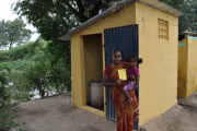 A woman holding her child in front of the toilet in her home in India. Photo Credit: Water.org.