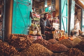 A young man sitting in front of piles of spices in his spice shop.