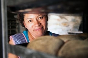 Mujer sonríe entre estantes con pan horneado en México.